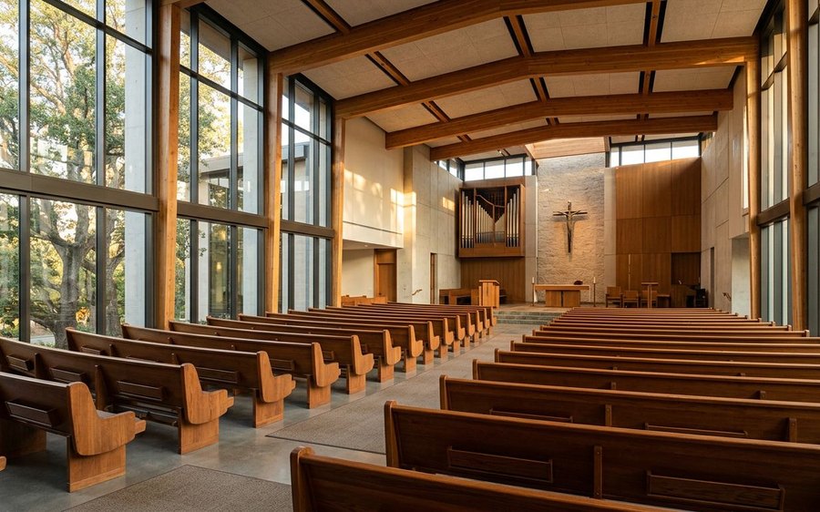 Modern church sanctuary with wooden pews and tall windows in late-day light