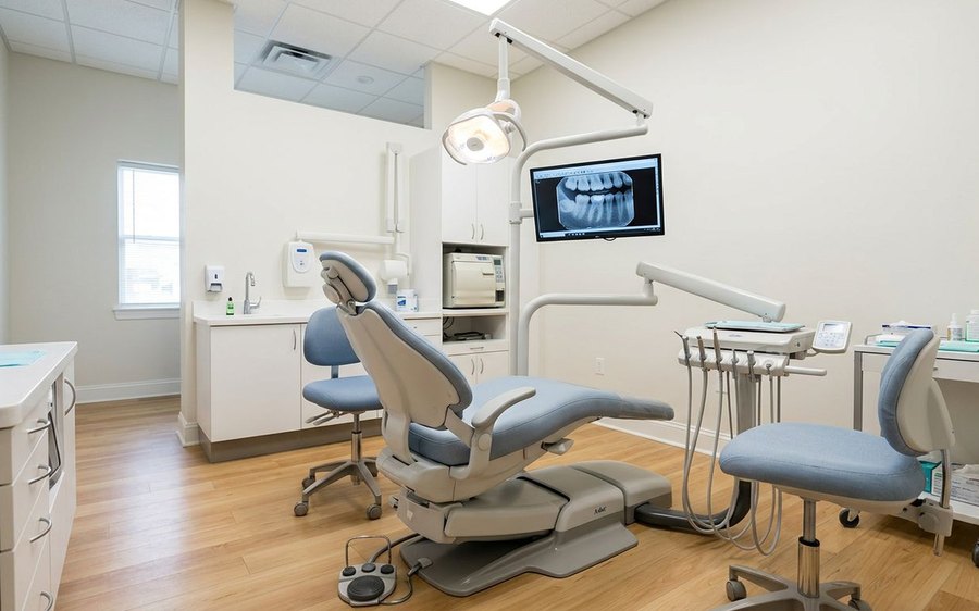 Modern dental treatment room with a patient chair, overhead light, and monitor
