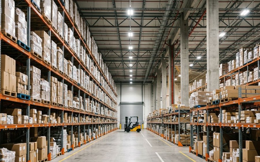 Warehouse aisle with tall pallet racking and a forklift at the end